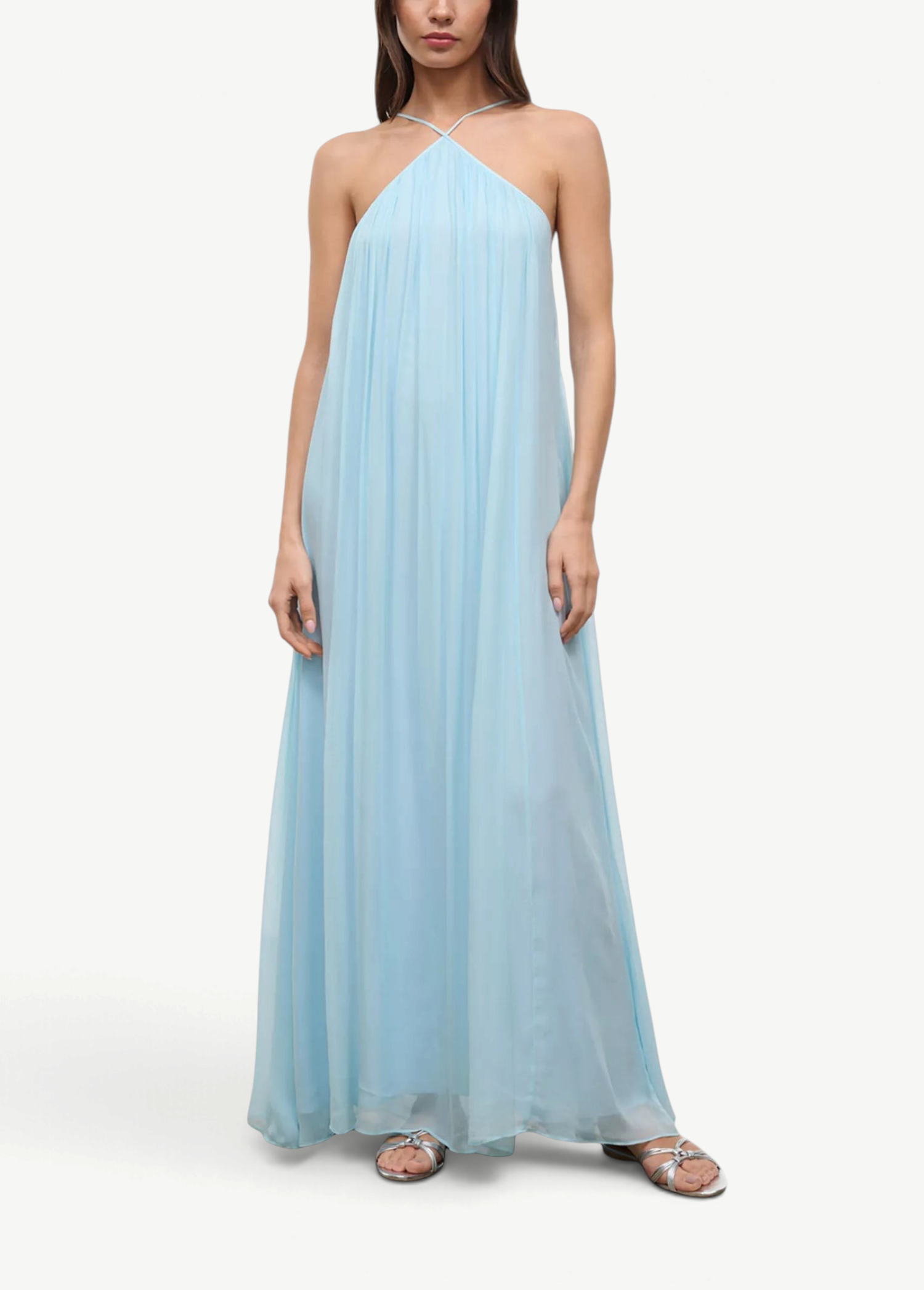 A floor-length, light blue Dasha Dress with a pleated halter-neck design, styled with silver strappy sandals for a minimalist summer look.