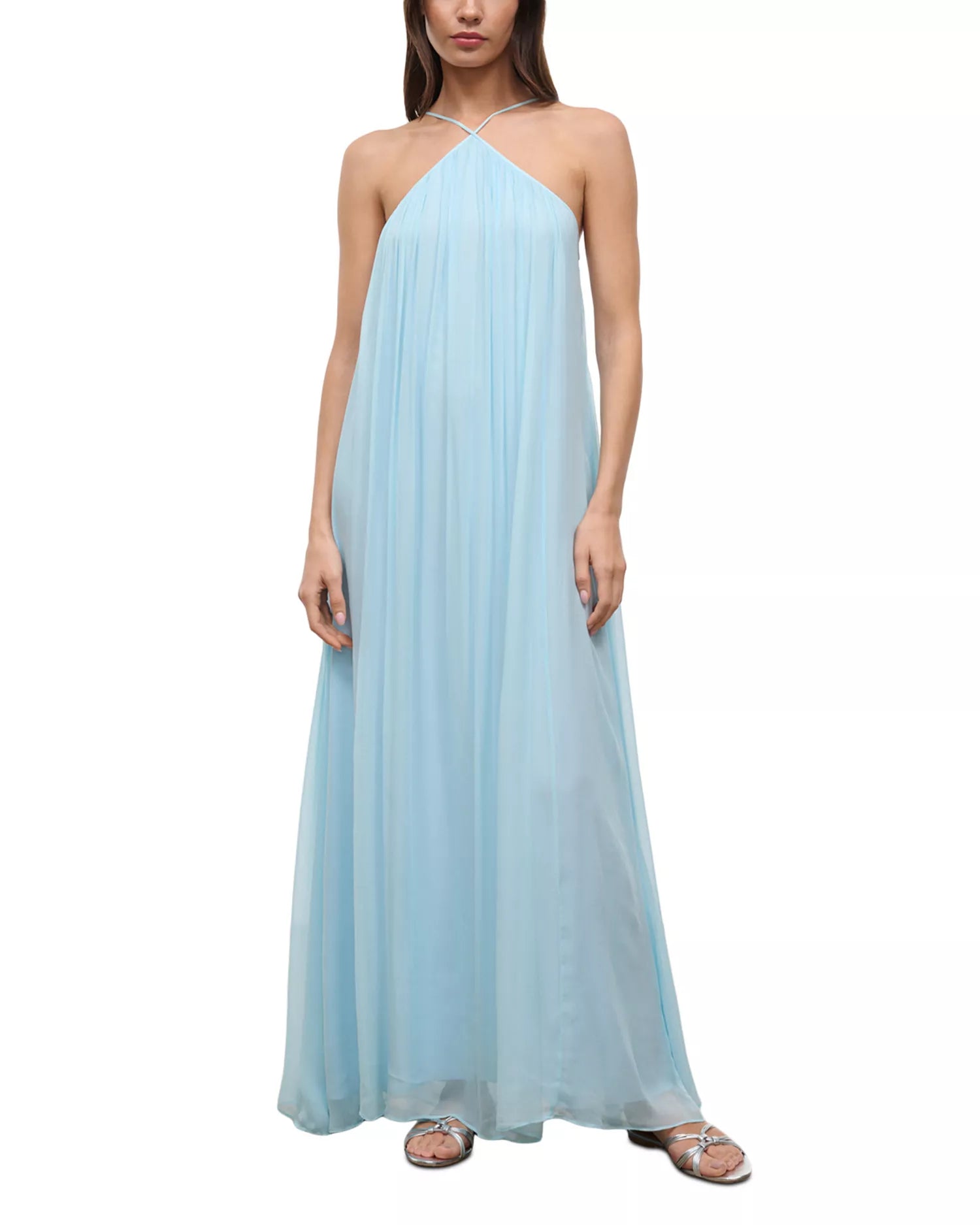 A floor-length, light blue Dasha Dress with a pleated halter-neck design, styled with silver strappy sandals for a minimalist summer look.