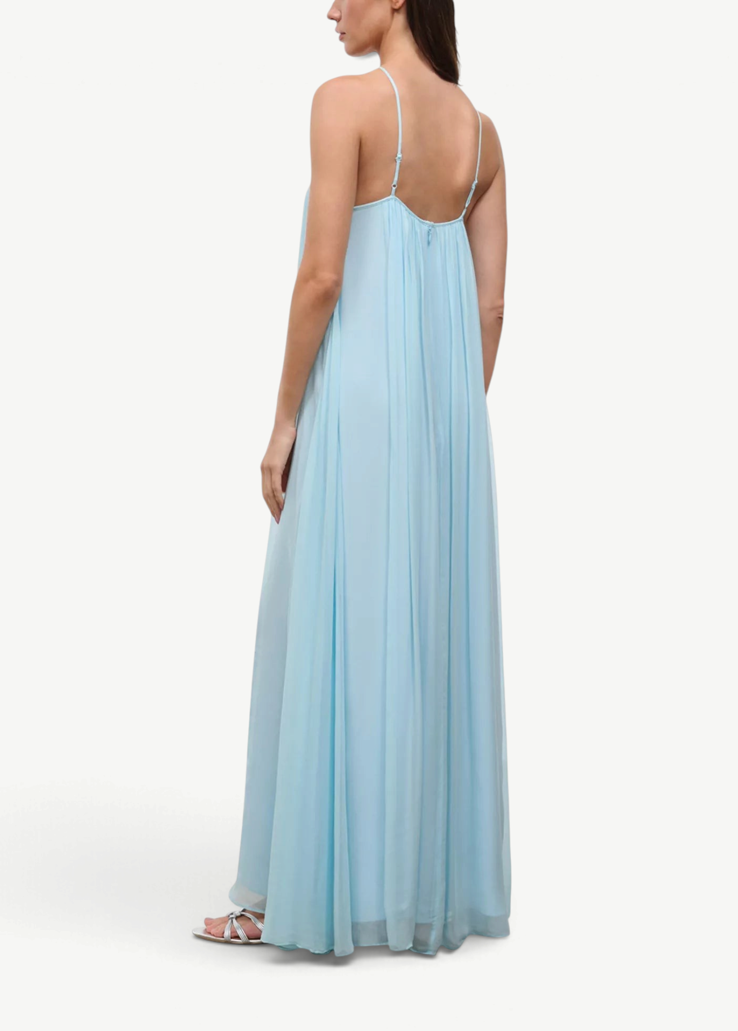 A person wearing a light blue, floor-length Dasha Dress with a minimalist design and spaghetti straps.