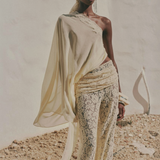 A person wears a one-shoulder pale yellow top with a draped sleeve, paired with vintage-inspired Rocio Trouser lace trousers and a matching lace headpiece.