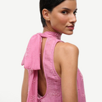A person wears the pink Mini Albee Dress, an elegant mini dress featuring a sophisticated silhouette with a high neck, open back, and beaded floral embroidery.