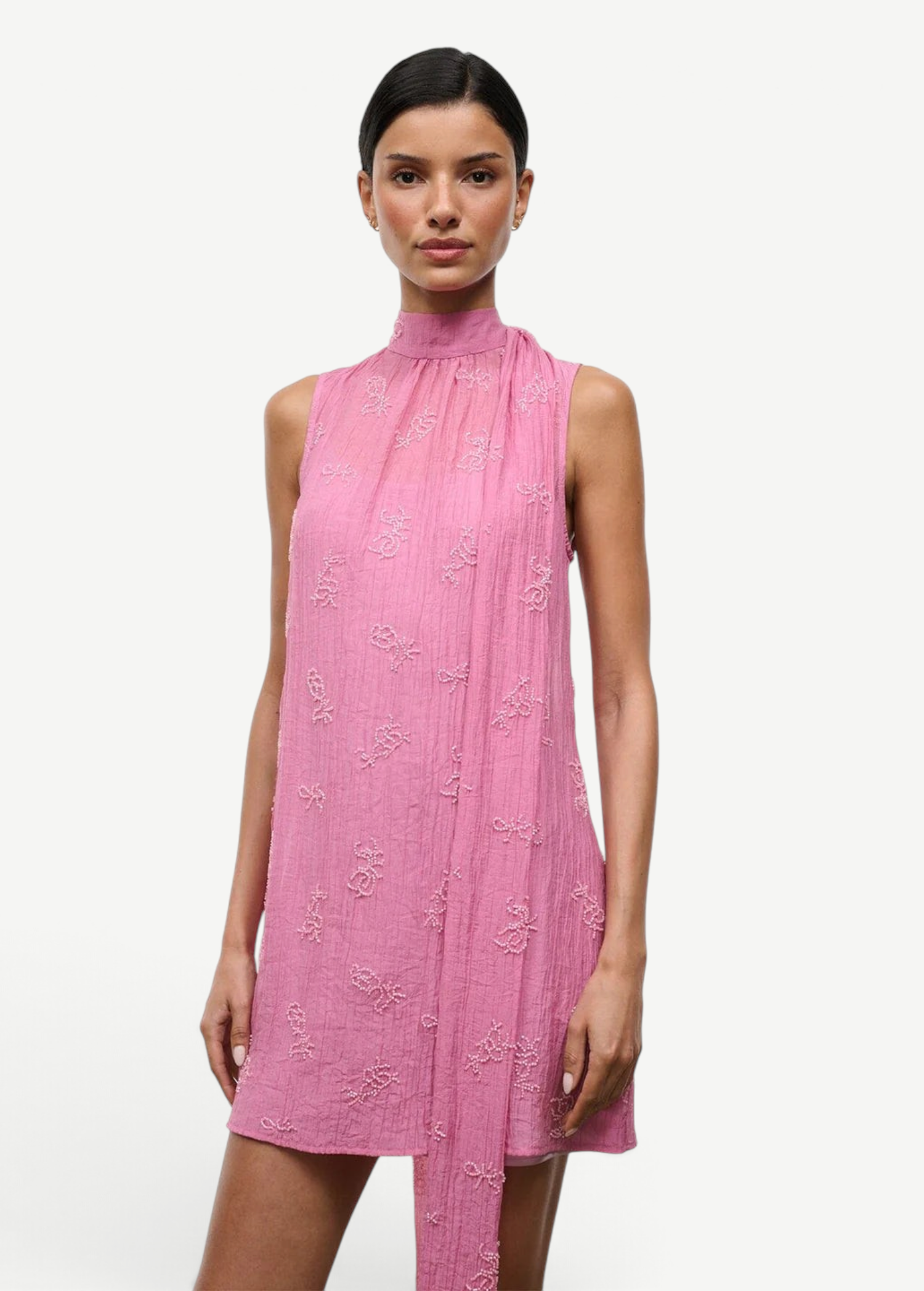 The Mini Albee Dress is a sleeveless, high-neck mini dress in pink featuring textured floral embroidery and an attached side scarf for a sophisticated silhouette.