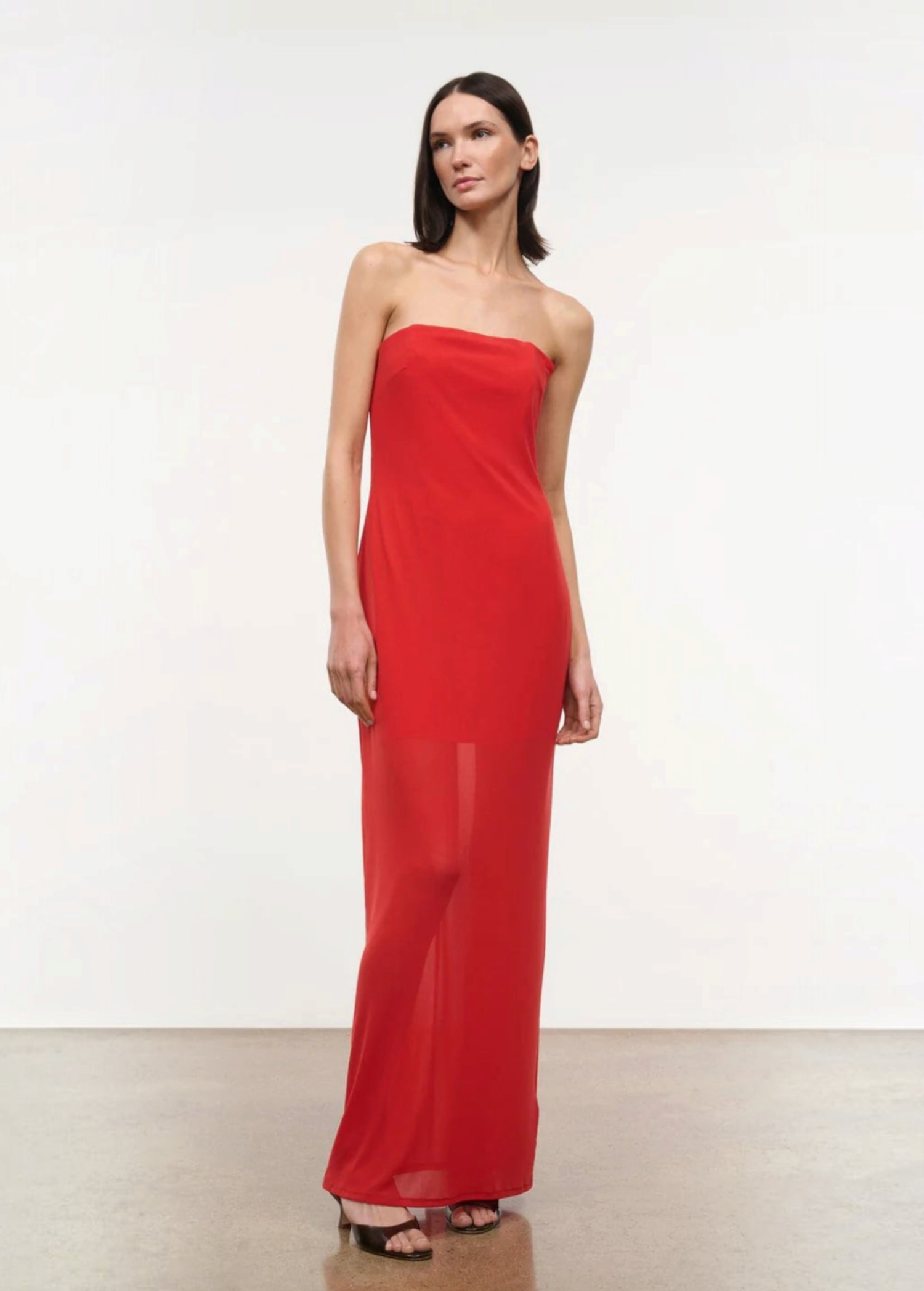 A person wearing a red, floor-length, strapless Liliana Dress with a sheer overlay.