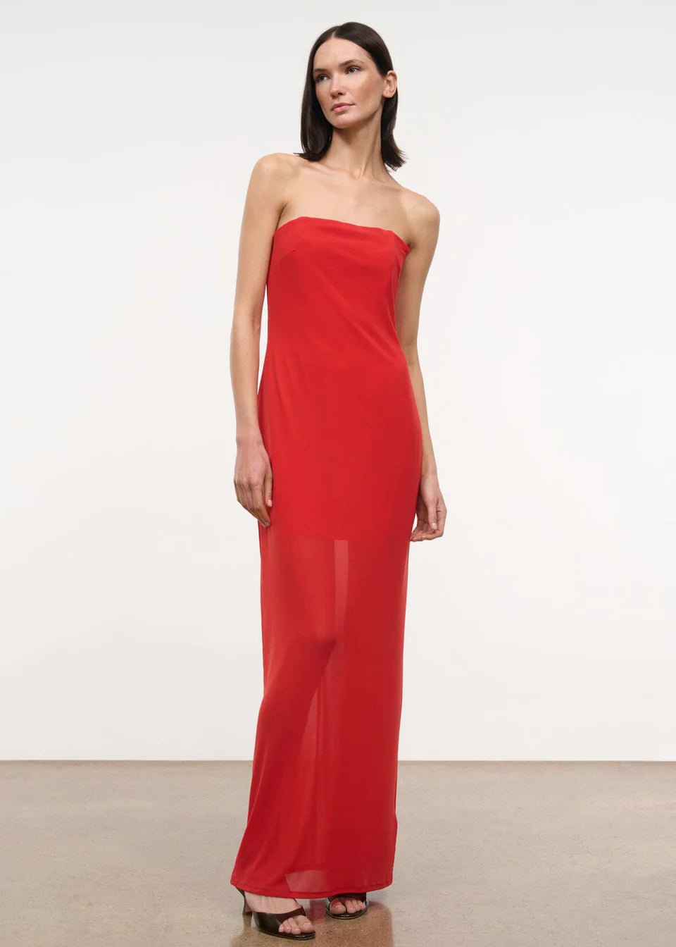 A person wearing a red, floor-length, strapless Liliana Dress with a sheer overlay.