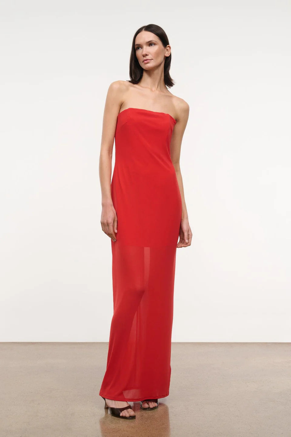 A person wearing a red, floor-length, strapless Liliana Dress with a sheer overlay.