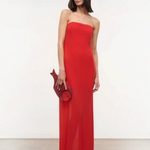 A person wears a red floor-length Liliana Dress styled with a matching fish-shaped clutch for a special occasion.