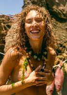 KABE SHOP INC Tesoro necklace featuring mixed natural beads of wood, coconut, seashell, and stone on a smiling woman