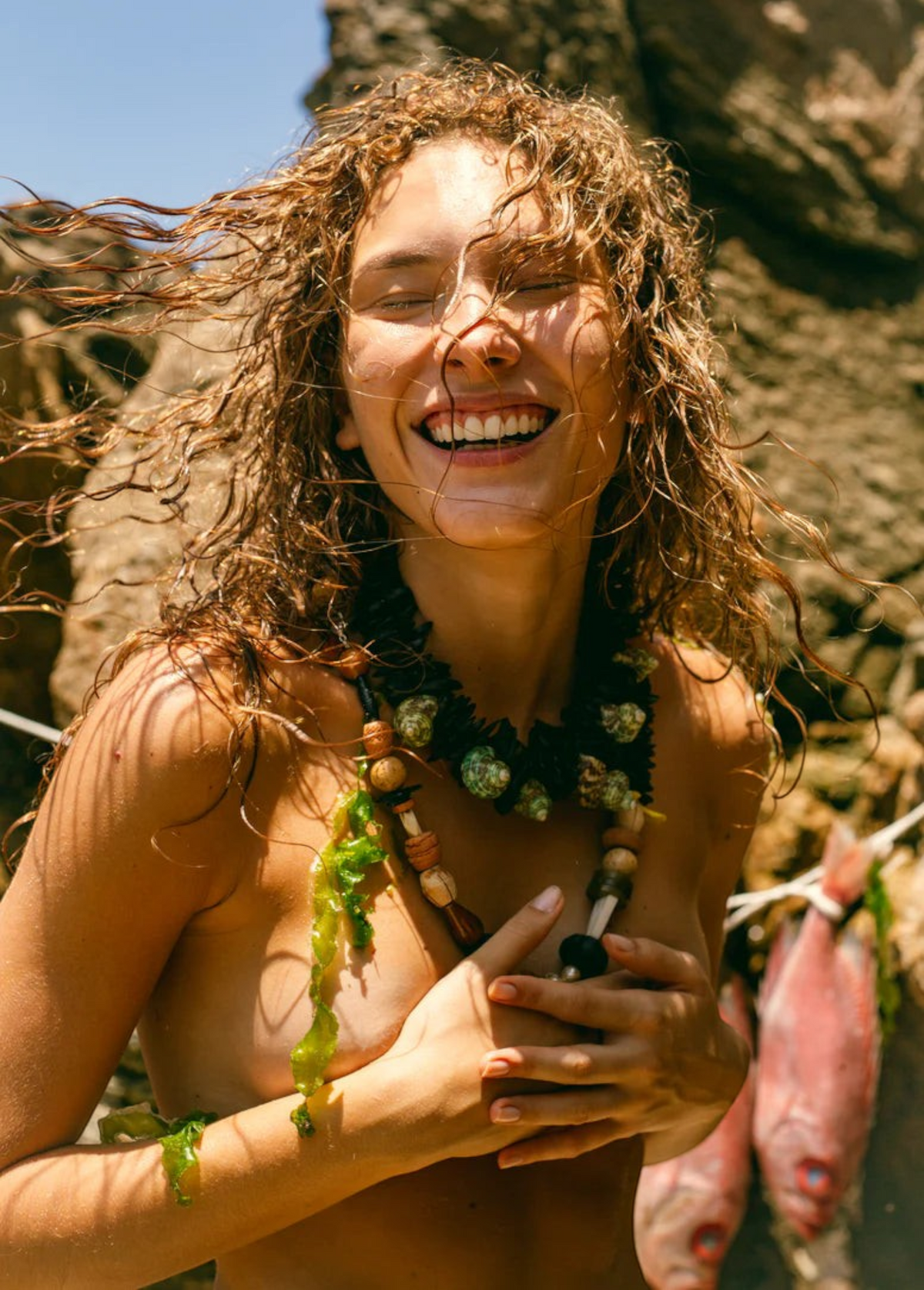 KABE SHOP INC Tesoro necklace featuring mixed natural beads of wood, coconut, seashell, and stone on a smiling woman