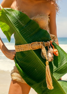 KABE SHOP INC Jibe belt in natural woven fiber with removable seashell charms and tassel, worn on a beach.