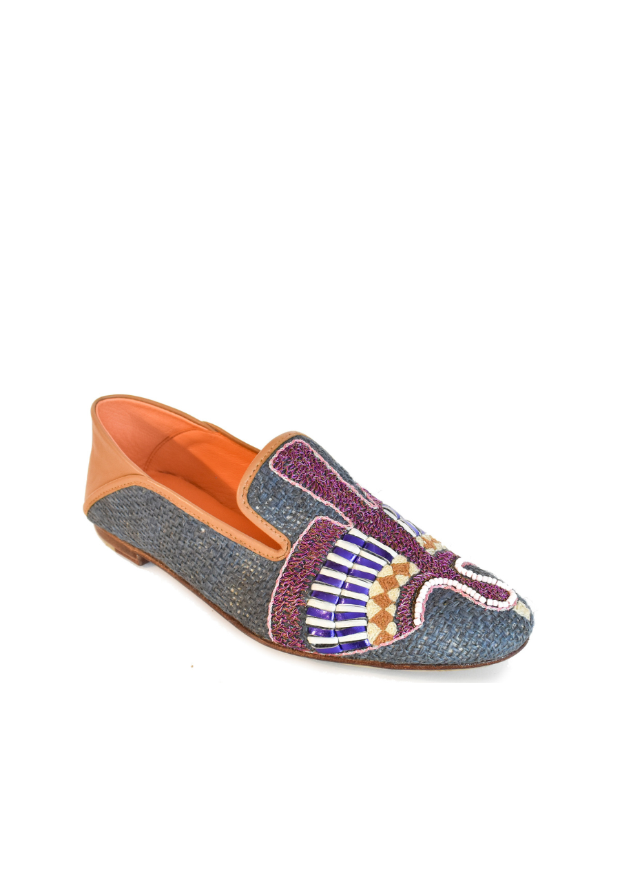 The Anzu Moccasin is a hand-embroidered leather loafer crafted with blue textured material, multicolored beaded designs on the upper, tan leather detailing at the heel, and an orange interior.