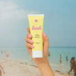 KABE SHOP INC SPF 50 sunscreen lotion in a yellow tube held by a hand against a blurred beach background.
