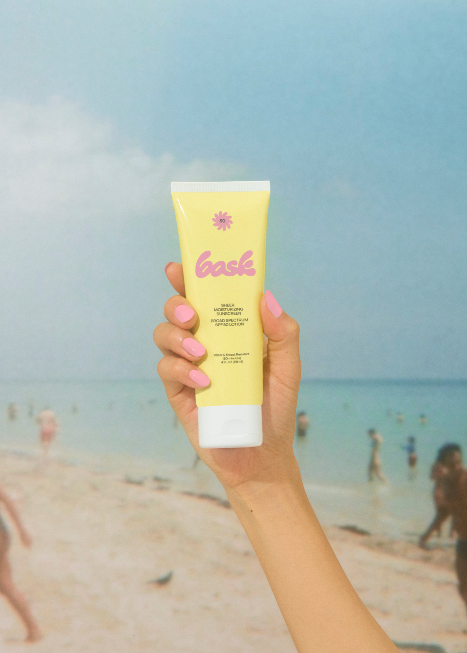 KABE SHOP INC SPF 50 sunscreen lotion in a yellow tube held by a hand against a blurred beach background.
