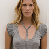 Wearing a short-sleeved, textured gray top, a person with long blonde hair stands against a plain white background looking directly at the camera, showcasing the Lariat Necklace White Bronze with its adjustable length.