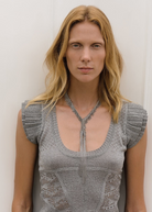 Wearing a short-sleeved, textured gray top, a person with long blonde hair stands against a plain white background looking directly at the camera, showcasing the Lariat Necklace White Bronze with its adjustable length.