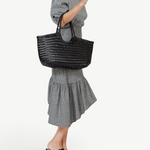 KABE SHOP INC Nantucket Basket Big black handwoven buffalo calf leather tote bag carried by a woman in a gingham dress