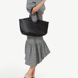 KABE SHOP INC Nantucket Basket Big black handwoven buffalo calf leather tote bag carried by a woman in a gingham dress