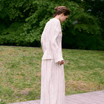 A person wearing a Kiki Shirt with metallic detailing and a matching pleated skirt stands on an outdoor wooden platform, creating a romantic silhouette.