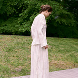 A person wearing a Kiki Shirt with metallic detailing and a matching pleated skirt stands on an outdoor wooden platform, creating a romantic silhouette.