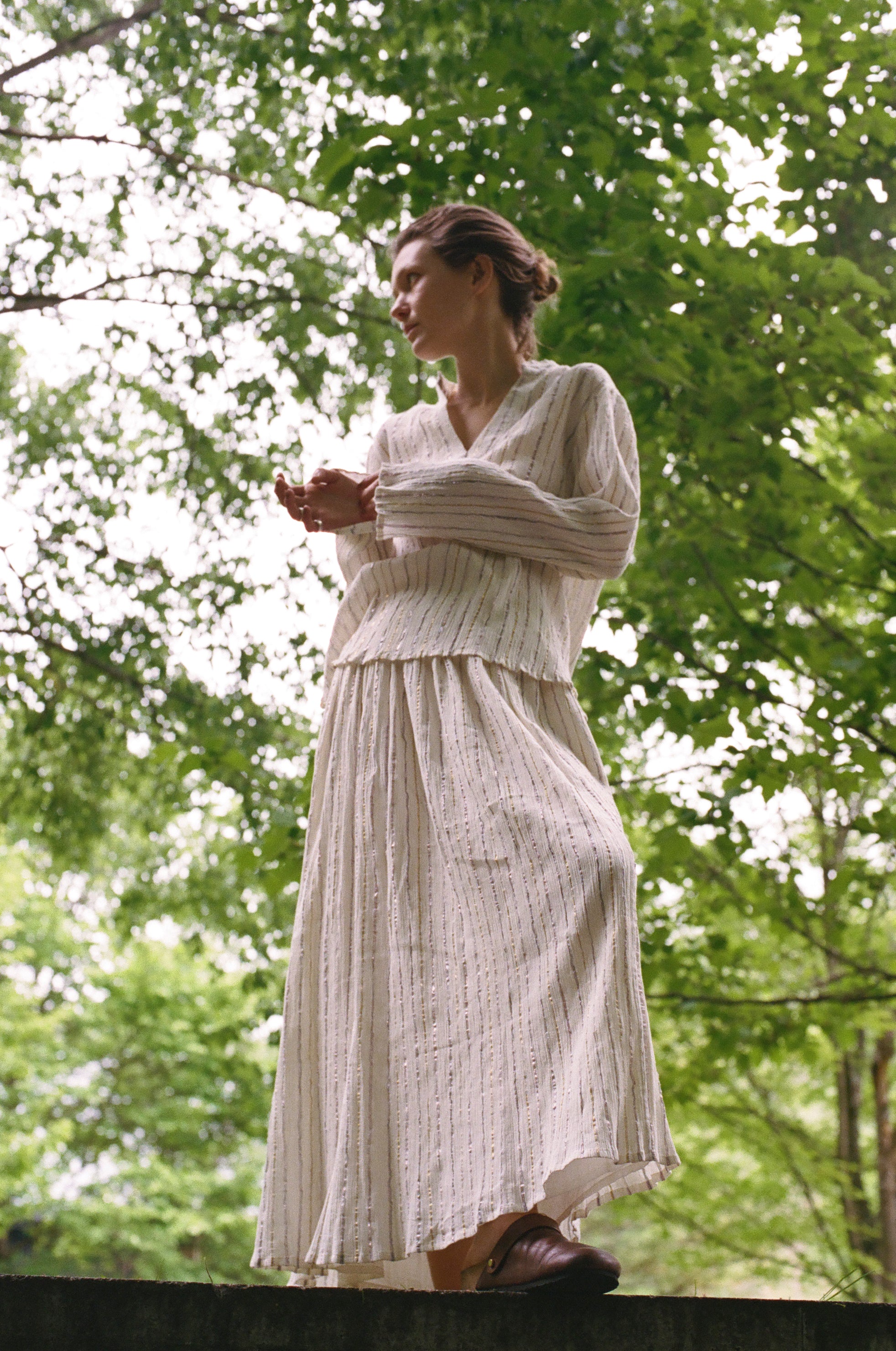 A person wearing a Kiki Shirt paired with a matching pleated skirt in cream fabric with thin metallic detailing, creating an elegant statement silhouette.