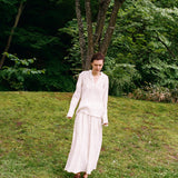 A person wearing an elegant pinstriped Kiki Shirt with a matching long skirt stands on a grassy slope, creating a romantic silhouette.