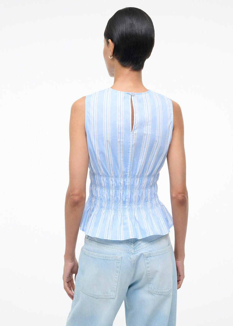 Back view of the Culver Top, a feminine, sleeveless blue and white striped peplum top with a smocked waist and a small keyhole opening at the nape of the neck for a flattering silhouette.