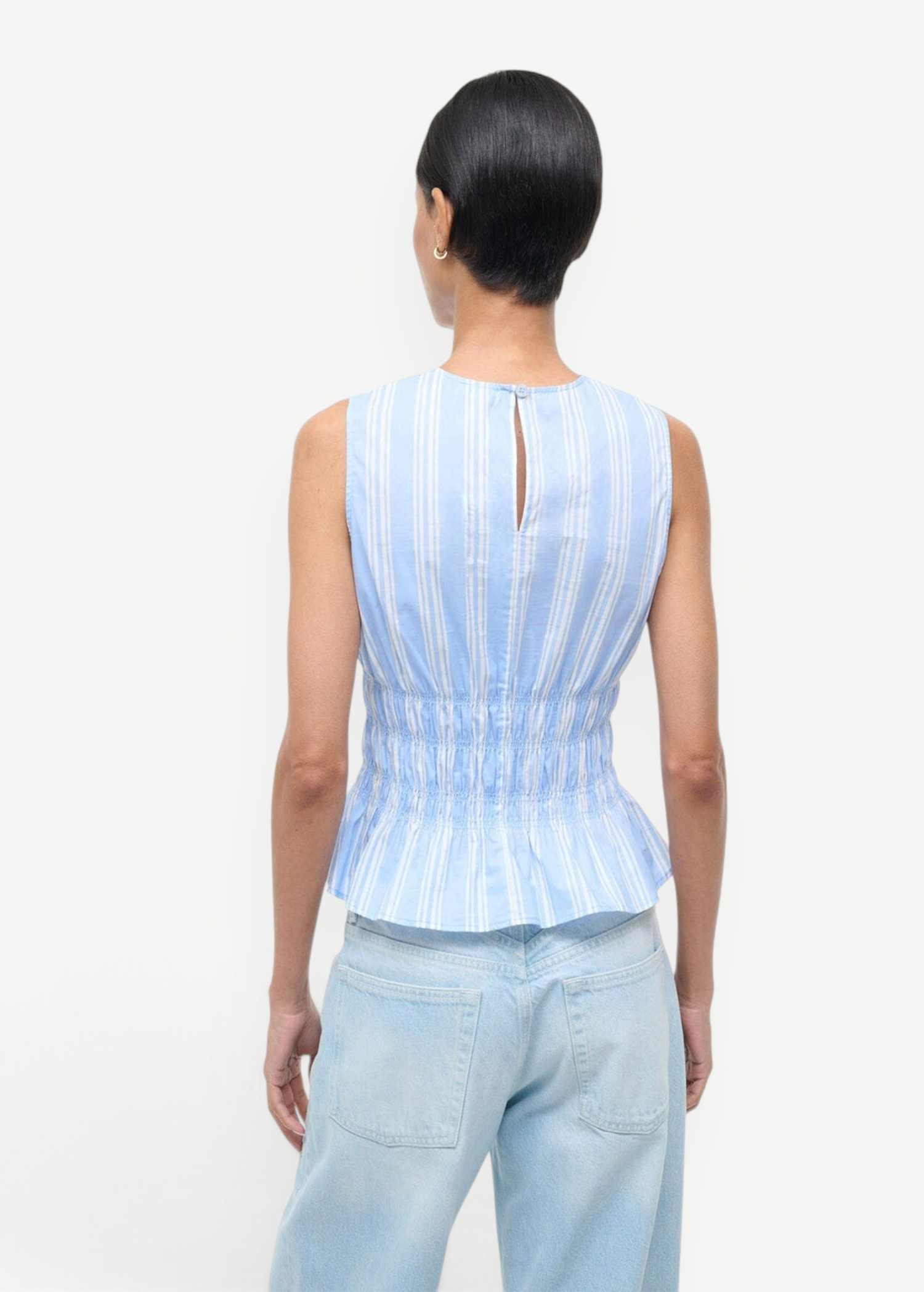 Back view of the Culver Top, a feminine, sleeveless blue and white striped peplum top with a smocked waist and a small keyhole opening at the nape of the neck for a flattering silhouette.