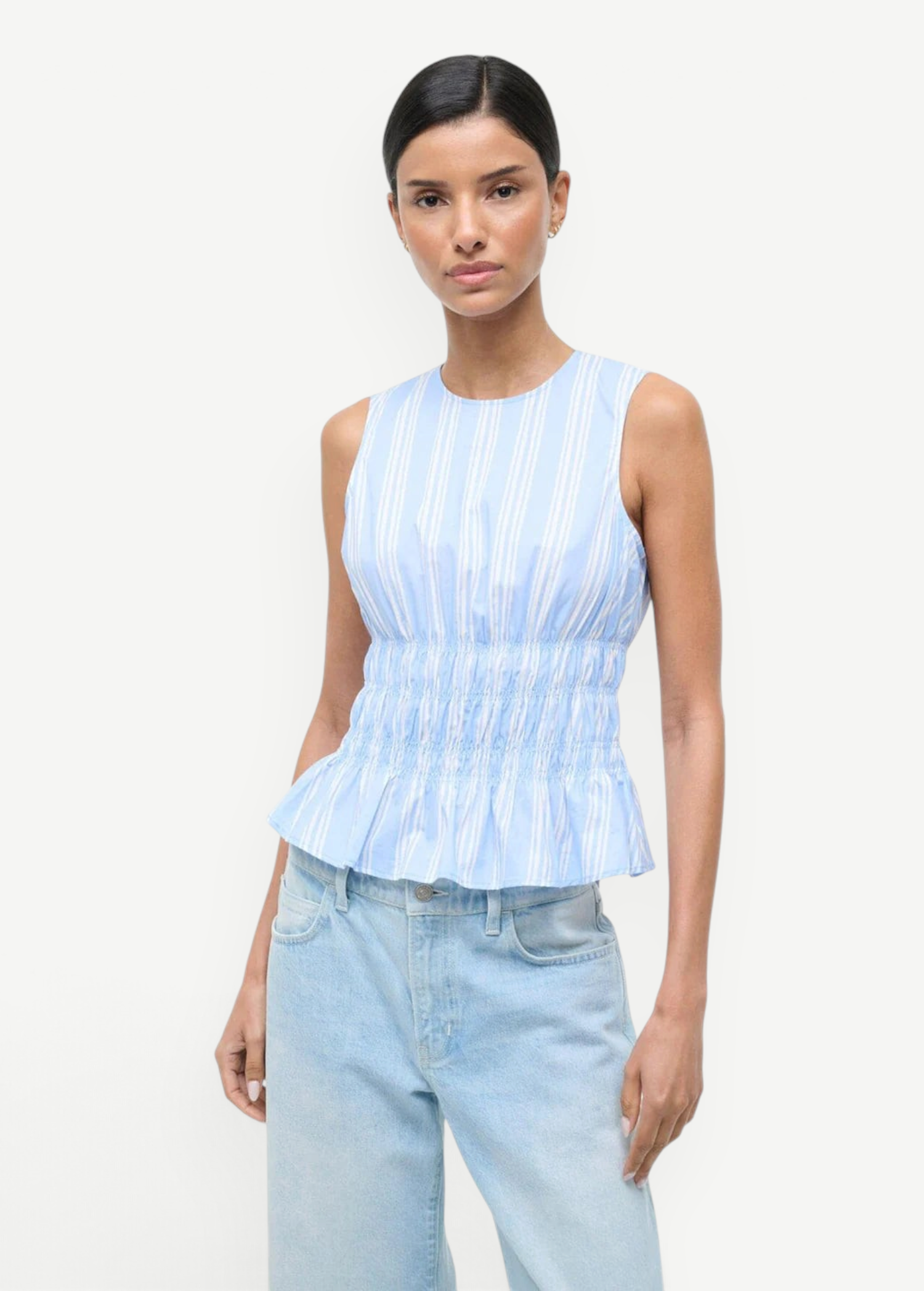 Culver Top in a light blue and white striped sleeveless peplum style with a smocked waist for a feminine silhouette.