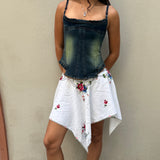 A woman stands against a beige wall wearing a denim corset top and the Celia Dragouni x KABE Embroidered Mini Skirt, her hands casually resting in her pockets.
