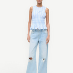 Culver Top featuring a sleeveless, blue-and-white striped peplum design with a smocked waist, paired with light-wash, ripped wide-leg jeans.