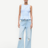 Culver Top featuring a sleeveless, blue-and-white striped peplum design with a smocked waist, paired with light-wash, ripped wide-leg jeans.