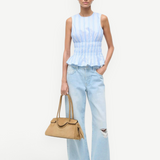 A model wears the light blue and white striped Culver Top with a sleeveless, smocked-waist silhouette, paired with light-wash distressed jeans and a tan handbag for a feminine style.