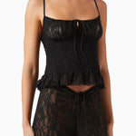 A woman wears the Slip Top—a black lace slip top with adjustable shoulder straps, a tied detail at the bust, and a slightly ruffled hem—paired with matching black lace pants featuring a tie at the waist.