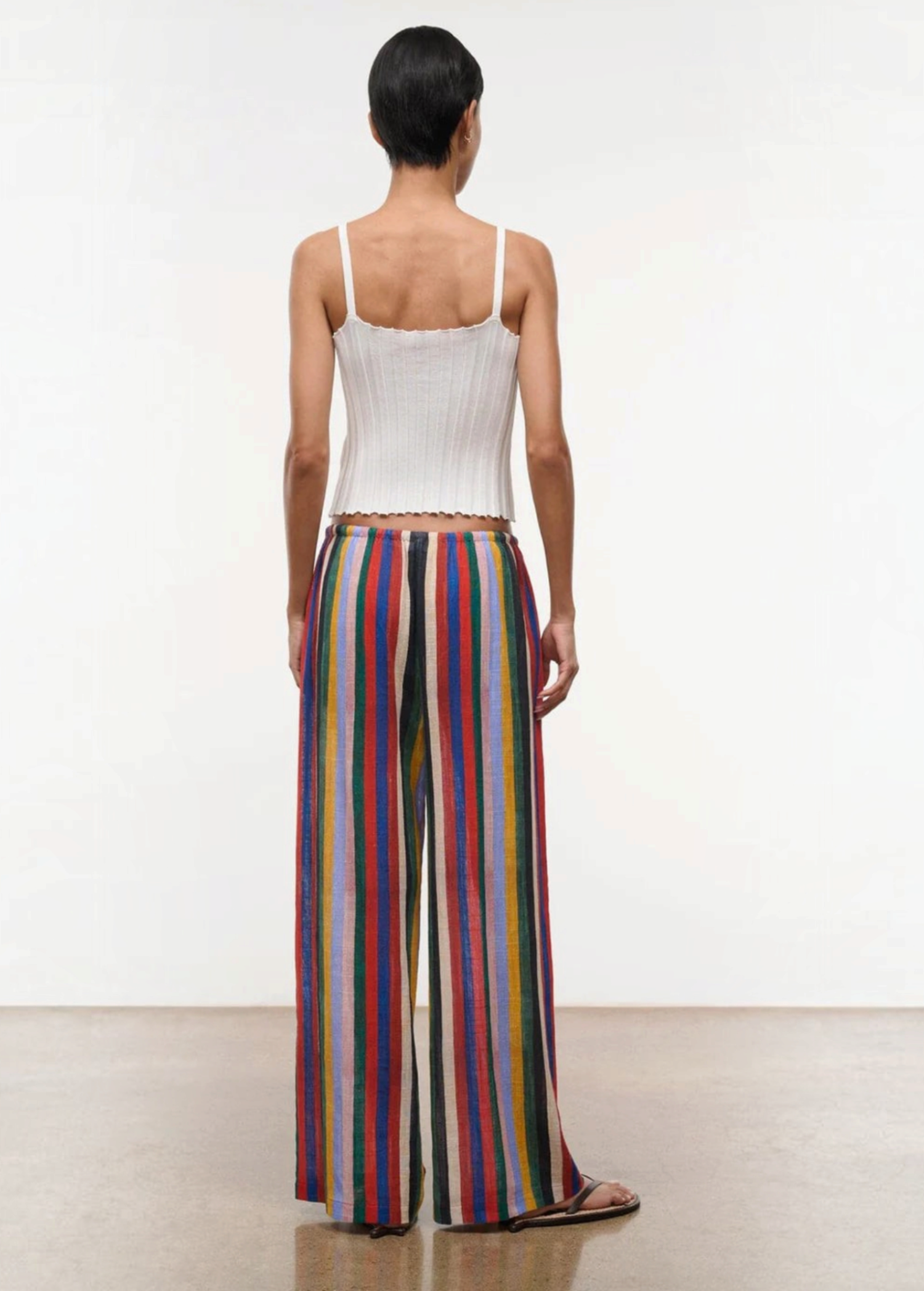 Back view of a person in a white ribbed tank top and Mateo Pant wide-leg trousers featuring vertical multicolored stripes.