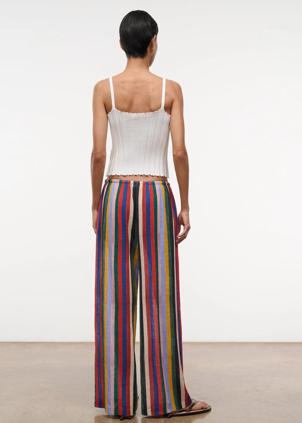 Back view of a person in a white ribbed tank top and Mateo Pant wide-leg trousers featuring vertical multicolored stripes.
