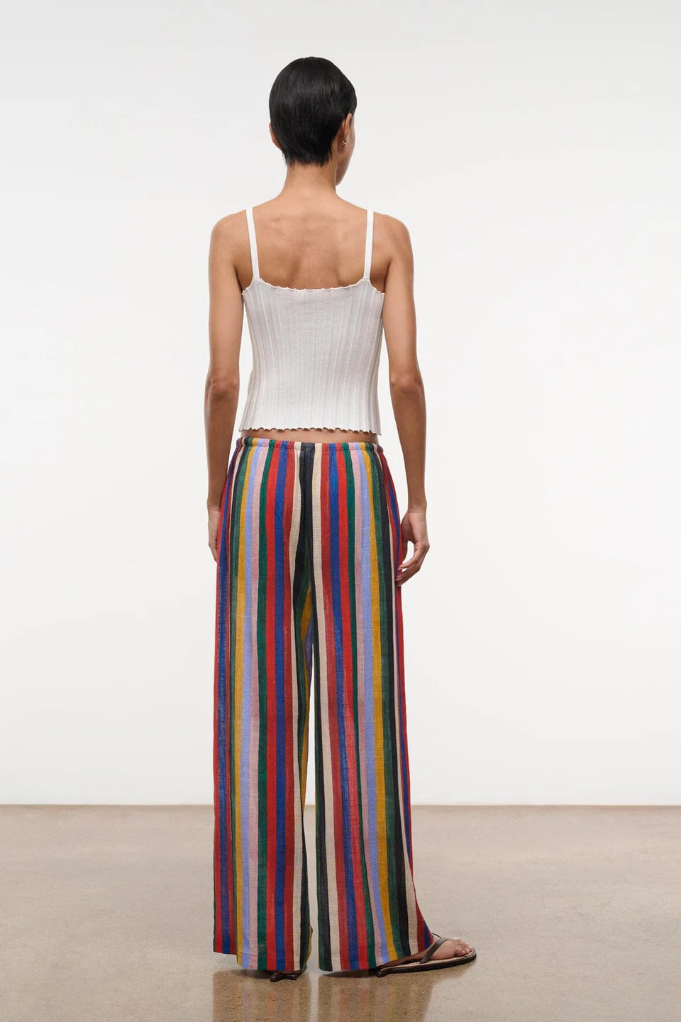 Back view of a person in a white ribbed tank top and Mateo Pant wide-leg trousers featuring vertical multicolored stripes.
