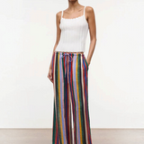 A model wears a white ribbed tank top with the Mateo Pant, which are relaxed high-waisted, wide-leg pants featuring vertical multicolored stripes and a drawstring waist.