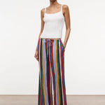 A model wears a white ribbed tank top with the Mateo Pant, which are relaxed high-waisted, wide-leg pants featuring vertical multicolored stripes and a drawstring waist.