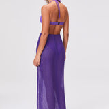 A woman stands with her back to the camera, wearing a purple halter bikini top and the Sarong Skirt in Blueberry Sorrento Gauze, paired with flat sandals, set against a plain light background.
