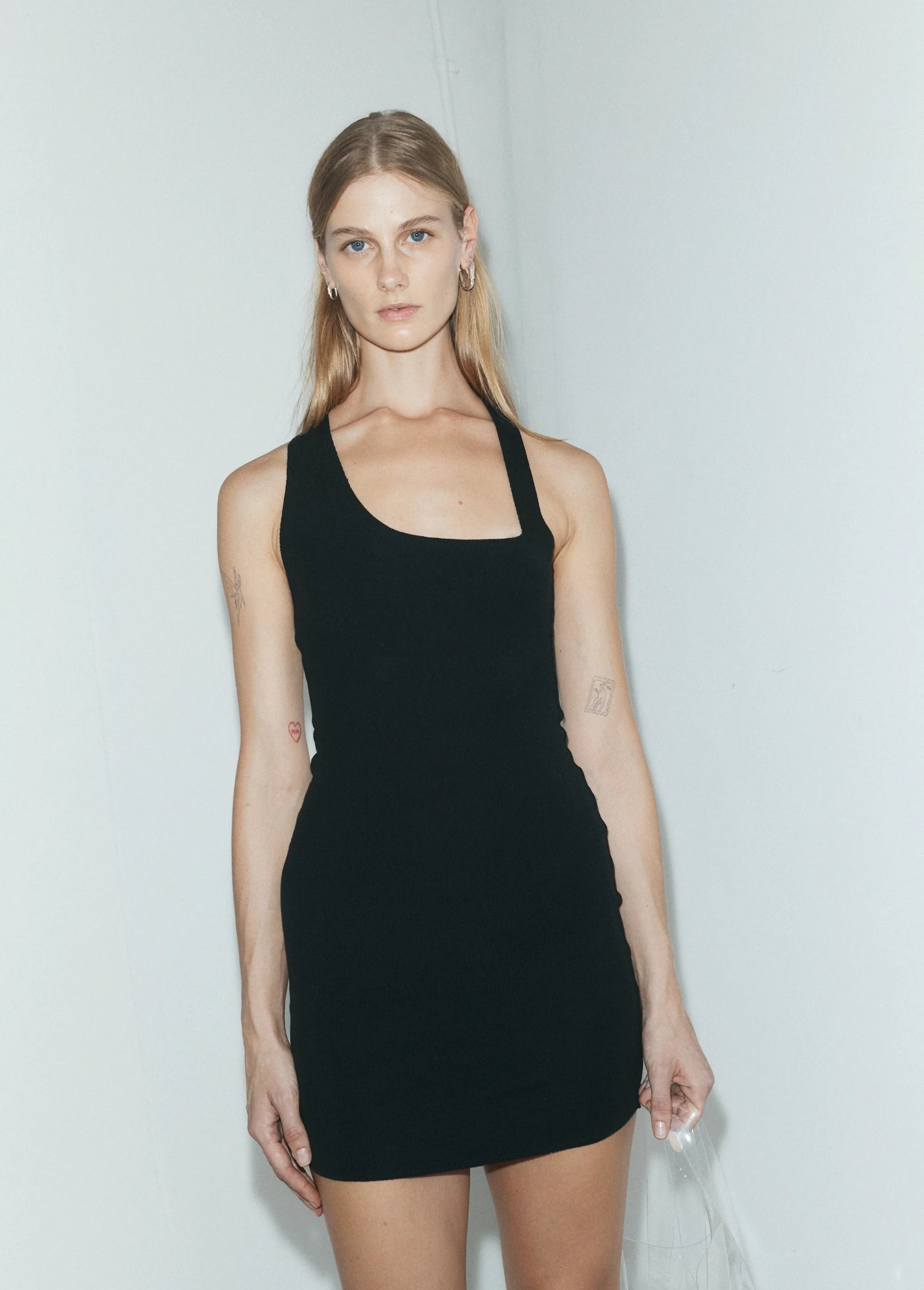 Model wearing a KABE SHOP INC black asymmetric racer mini slip dress with a body-hugging fit against a white wall.