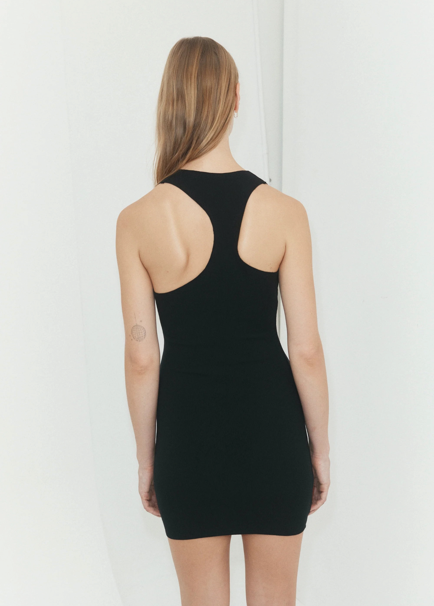 Back view of a woman wearing a KABE SHOP INC black asymmetric racerback mini slip dress with a body-hugging fit.