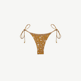 Praia Bottom: A gold beaded bikini bottom featuring a delicate white floral print, thin adjustable side ties embellished with beads, and a high-cut silhouette, made from recycled nylon swimwear material and showcased on a plain white background.