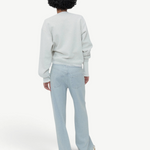 Wearing Cool Jeans in the softest denim, a person with short curly hair stands facing away, paired with a light grey sweatshirt against a plain, light grey background.