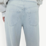 A person wearing Cool Jeans in a light-wash, relaxed-leg style made from the softest denim, paired with a light gray sweatshirt; shown from the back with the jeans’ back pockets clearly visible.