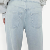 A person wearing Cool Jeans in a light-wash, relaxed-leg style made from the softest denim, paired with a light gray sweatshirt; shown from the back with the jeans’ back pockets clearly visible.
