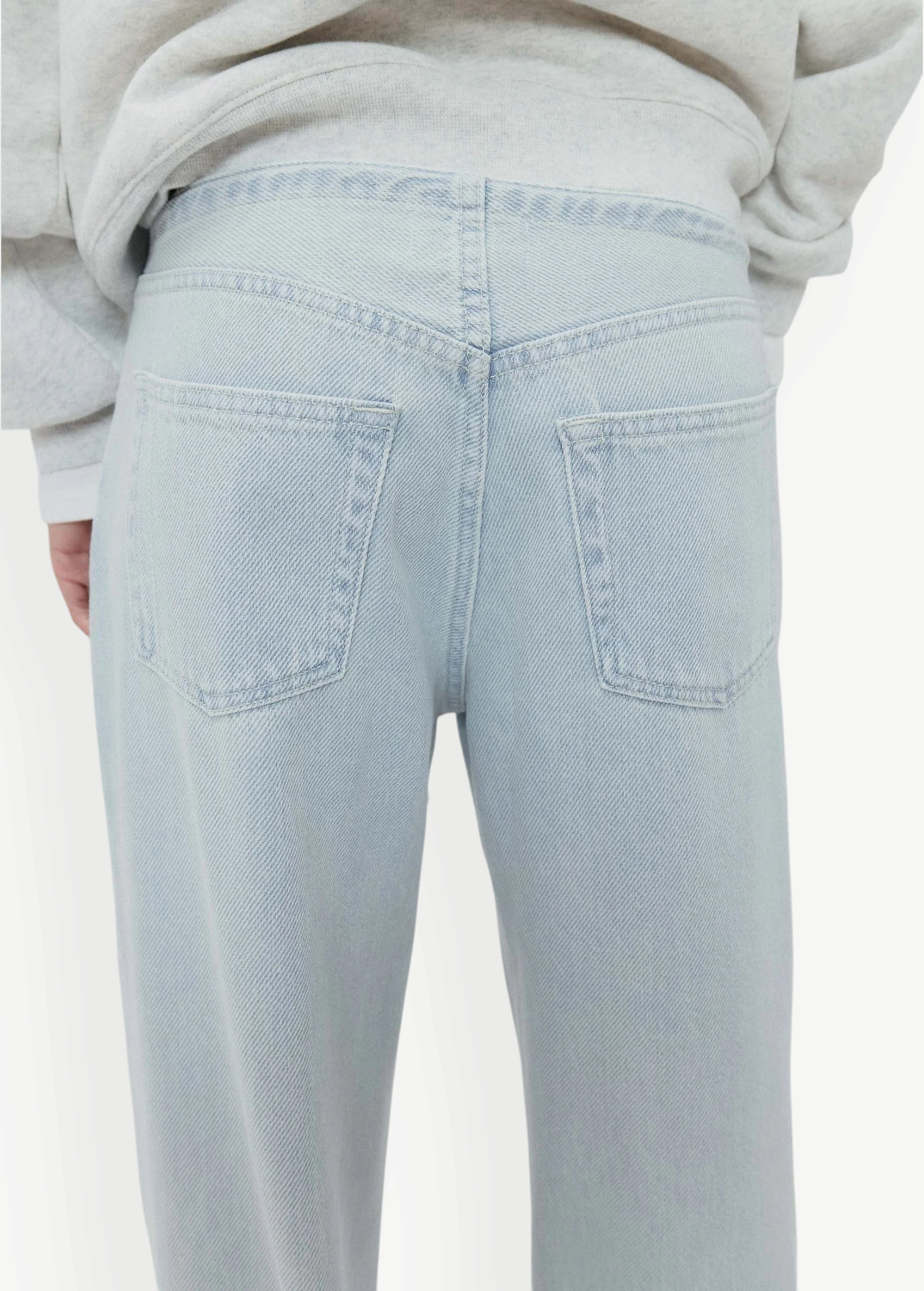 A person wearing Cool Jeans in a light-wash, relaxed-leg style made from the softest denim, paired with a light gray sweatshirt; shown from the back with the jeans’ back pockets clearly visible.