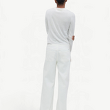 A person with short dark hair stands facing away, wearing a long-sleeve white shirt and the Cool Jean—a relaxed leg jean featuring an adjustable drawstring waist—set against a plain, light background.
