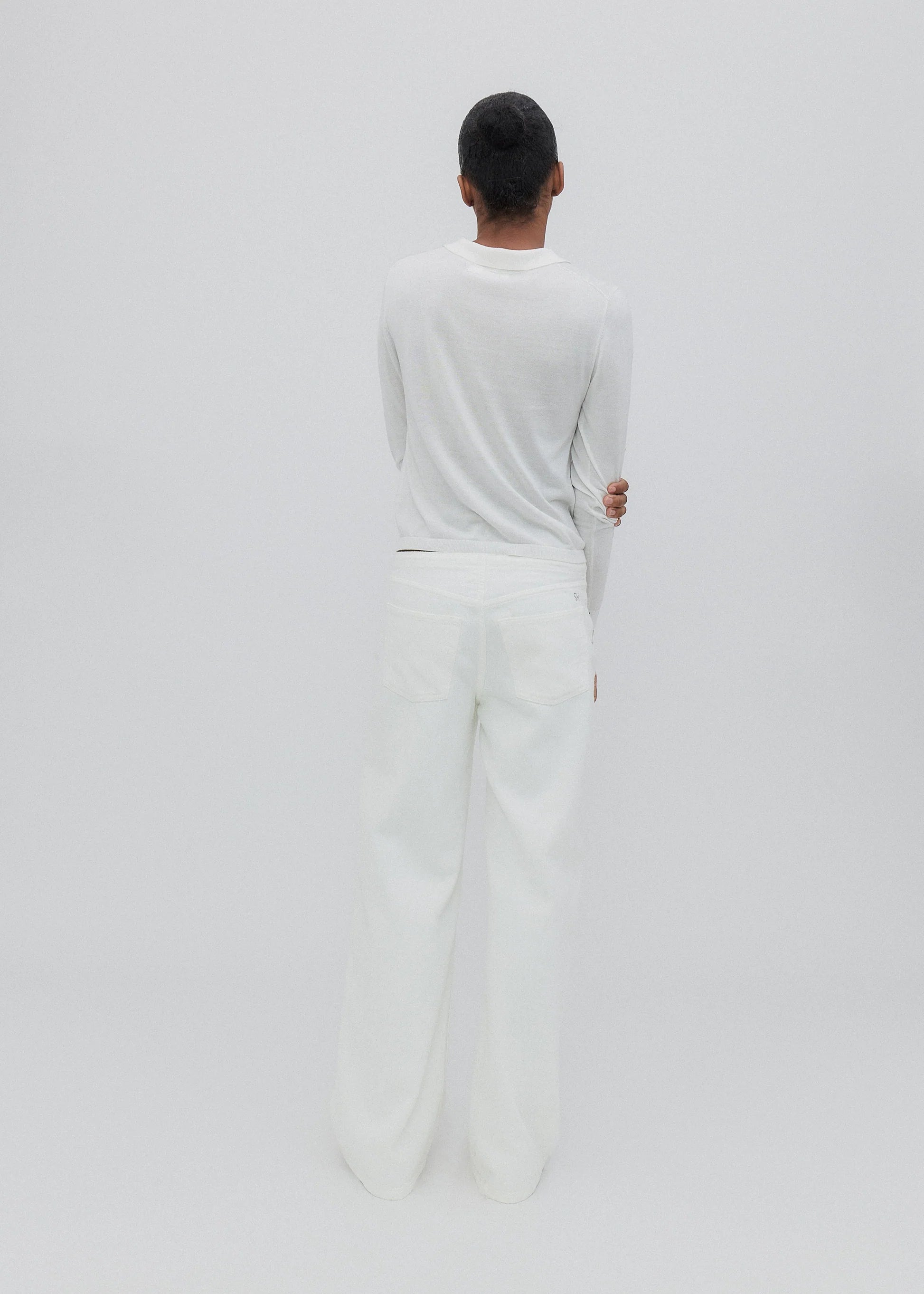A person with short dark hair stands facing away, wearing a long-sleeve white shirt and the Cool Jean—a relaxed leg jean featuring an adjustable drawstring waist—set against a plain, light background.