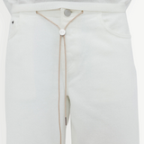 Wearing the Cool Jean in an off-white shade with a matching top, this look is cinched at the waist with a beige string belt featuring a round metallic front accent threaded through the waistband. The relaxed leg silhouette of the Cool Jean lends an effortlessly laid-back vibe to the outfit.
