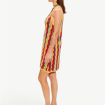 The Hazel Knit Dress is a sleeveless crochet mini dress featuring a colorful vertical zigzag pattern, worn with tan wedge sandals.