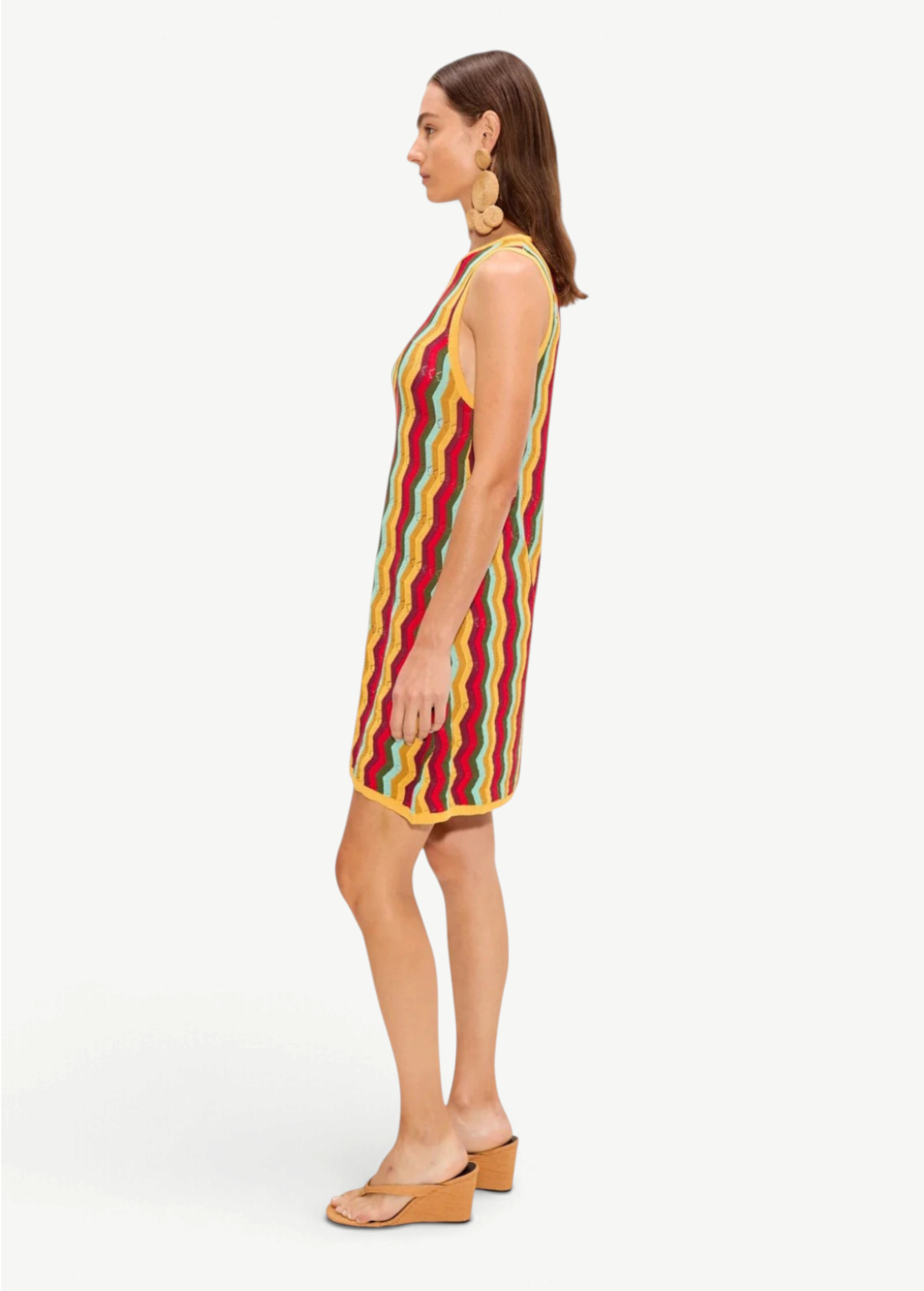 The Hazel Knit Dress is a sleeveless crochet mini dress featuring a colorful vertical zigzag pattern, worn with tan wedge sandals.